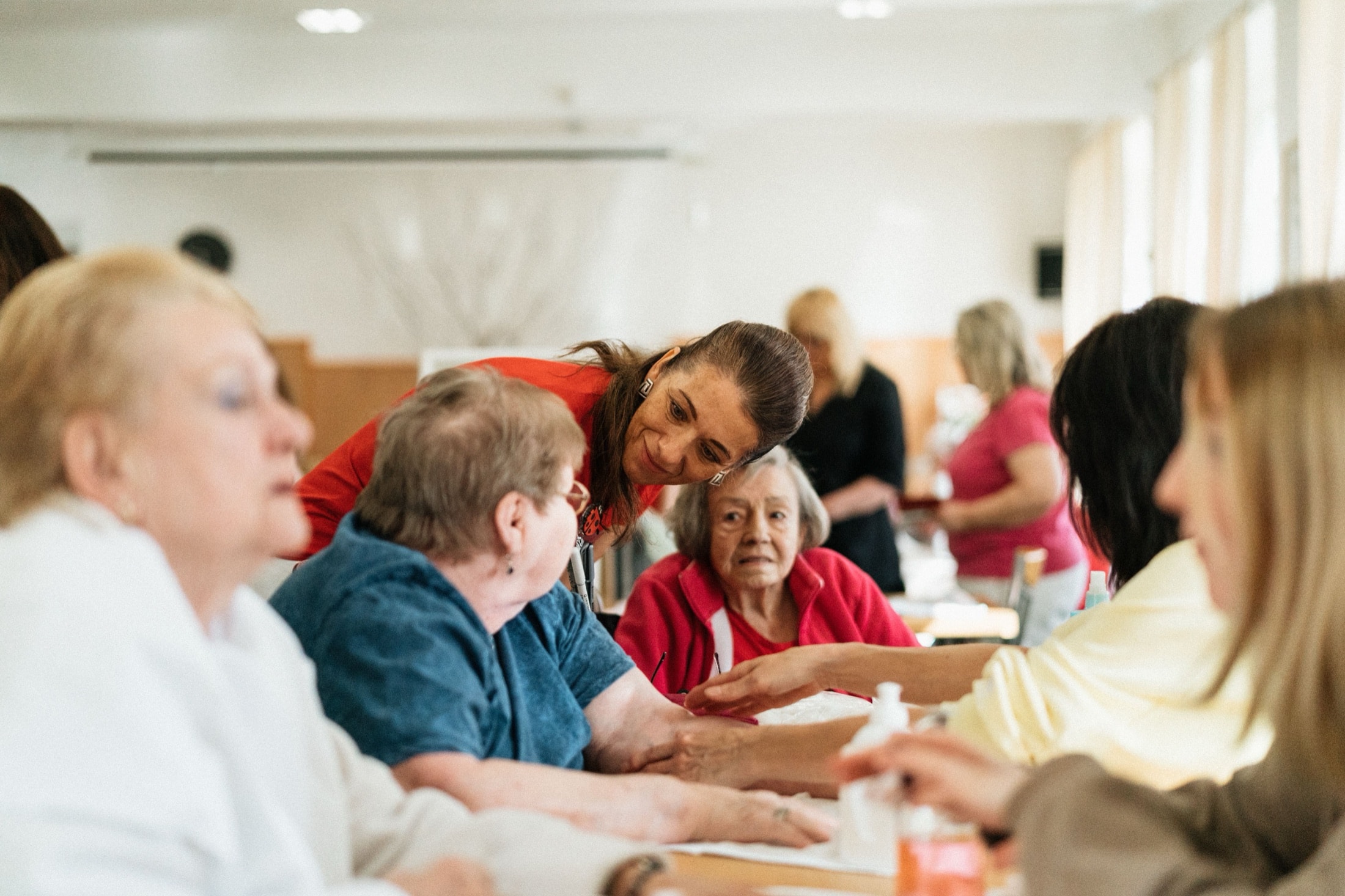 A caregiver leaning in to help two residents at an activity table